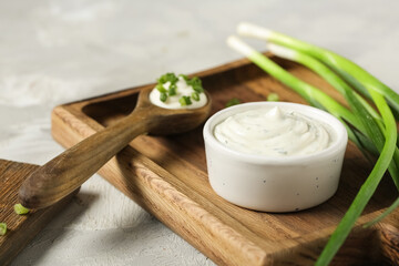 Cutting board with bowl and spoon of tasty sour cream and chopped green onion on grey grunge table