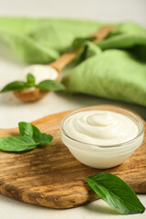 Cutting board with bowl of tasty sour cream and fresh basil on white grunge table