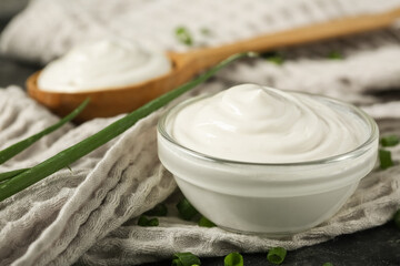 Napkin with bowl of tasty sour cream and fresh green onion, closeup