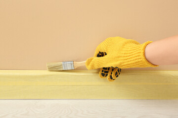 Decorator painting beige wall near masked baseboard, closeup