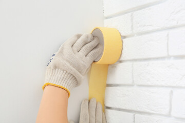 Woman applying masking tape to white wall, closeup