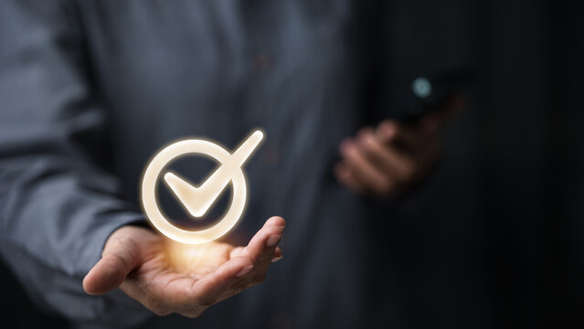 Glowing checkmark approval with smartphone in hand on dark background