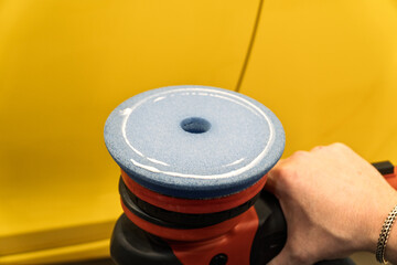 Car detailing series: Polishing yellow car. A master polishes the surface of a car body. Master repairman polishing body of car in workshop using polishing machine. Repair after an accident. PDR. 