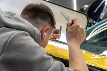 Process of paintless dent repair on car body. The mechanic at the auto shop with tools to repair dents in car body. Body repair. A specialist repairs a dent on the car body without painting. PDR.