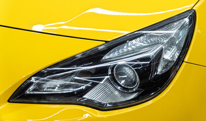 Close up detail on one of the LED headlights modern yellow car. Exterior closeup detail. Headlights of car. BI-LED headlights of a modern and expensive yellow car. Front BI-LED headlight on sport car.