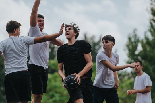 A group of young men play an outdoor basketball game, celebrating with high fives and teamwork while one player advances with the ball, showcasing friendship, fitness, and competitive energy.