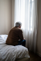 Sad old man in emotional numbness, physical fatigue and cognitive deterioration sit on bed and look...