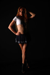 A red-haired, long-legged girl in a sailor costume poses standing in full length low key