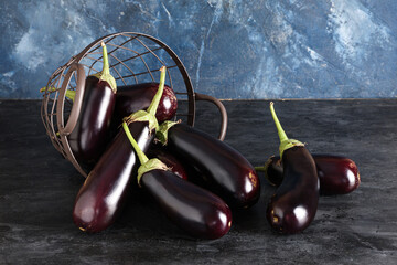 Overturned colander with fresh eggplants on blue grunge background, closeup
