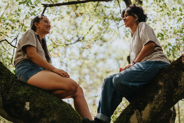 Two people relax on a sturdy tree branch in a sun-dappled forest, enjoying each others company. The scene captures friendship, outdoor leisure, and natural shade in a candid moment.