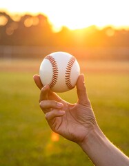 A hand holds a baseball at sunset