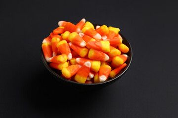Bowl with tasty Halloween candy corns on black background, closeup