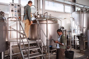 Brewery workers inspecting production quality control with digital tablet