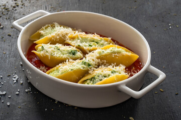 Pasta shells stuffed with cheese and spinach in tomato sauce in baking dish prepared for baking on black table