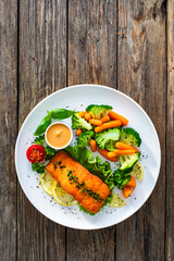 Fried salmon steak with boiled broccoli and mini carrots and mayonnaise on wooden table. Top view
