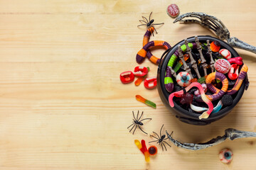 Composition with pot of treats for Halloween and skeleton hands on wooden background
