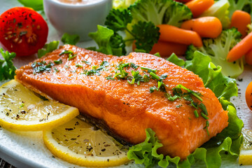 Fried salmon steak with boiled broccoli and mini carrots and mayonnaise on wooden table	