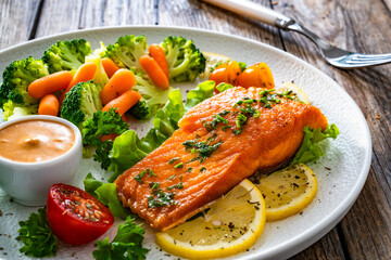 Fried salmon steak with boiled broccoli and mini carrots and mayonnaise on wooden table	