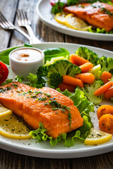 Fried salmon steak with boiled broccoli and mini carrots and sauce on wooden table	