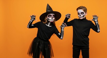Two children in skeleton costumes with sugar skull makeup for Halloween. Spooky boy and girl posing on an orange background. Day of the Dead party concept