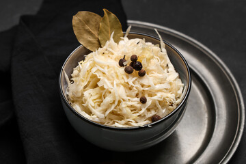 Bowl with tasty sauerkraut, peppercorns and bay leaves on black background, closeup
