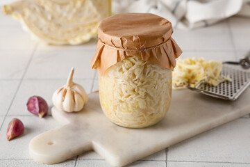 Jar with tasty sauerkraut and garlic on white tile background
