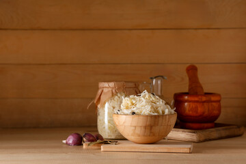 Bowl with tasty sauerkraut and different spices on wooden background