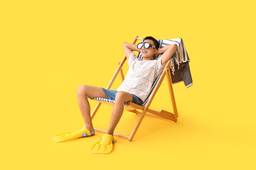 Young Asian man in swimming goggles and flippers sitting on deckchair against yellow background © Pixel-Shot
