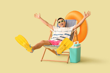 Young Asian man with beach cooler, flippers and inflatable ring sitting on deckchair against green background © Pixel-Shot