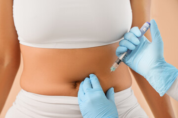 Doctor's hands injecting woman on beige background, closeup. Weight loss concept