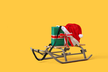 Sled with gift box and Santa hat on yellow background