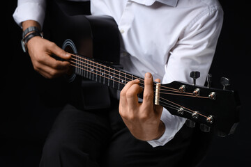 Fototapeta premium Young man playing guitar on black background