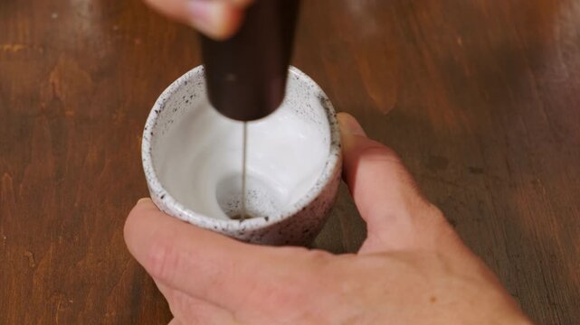 This is a demonstration showcasing the process of milk frothing using an electric frother placed in a ceramic cup