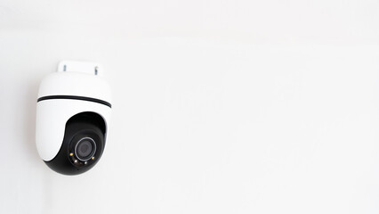 A camera is mounted on a wall. The camera is black and white. The camera is pointed at the viewer