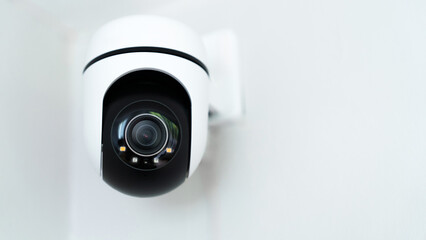 A camera is mounted on a wall. The camera is a dome shaped camera. The camera is black and white