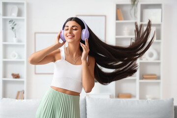 Beautiful young woman in modern headphones listening to music and dancing at home
