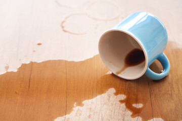 Overturned cup and spilled coffee on table in kitchen, closeup