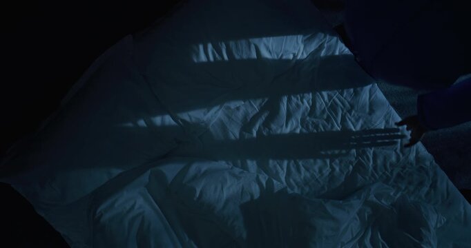 Mature man lies in bed, staring into darkness with deep existential thoughts. At night, man lost in thought. Concept of fear of aging, midlife crisis, loneliness, sleepless musings. Rotating Top View.