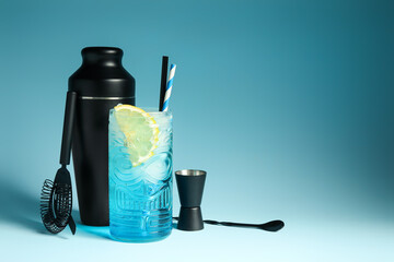 Glass of fresh cocktail and bartender tools on blue background