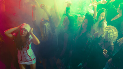 Girls in a crowd in Halloween costumes dancing with bright green neon lights. Concept of party...