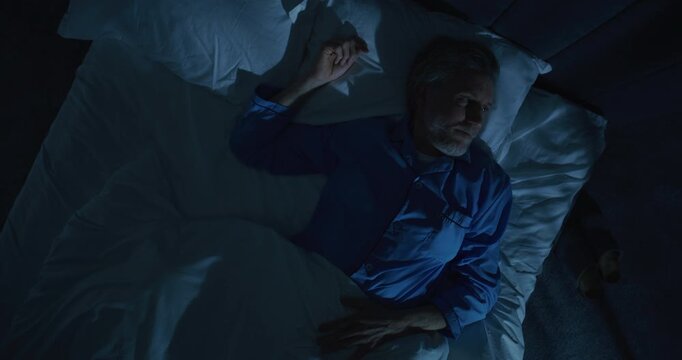 Middle Aged Man Lies Awake at Night in Silence, Tossing and Turning in Bed, Confronting Fear of Mortality, Passage of Time. Concept of Existential Musings, Midlife Crisis, Insomnia. Rotating Top View.