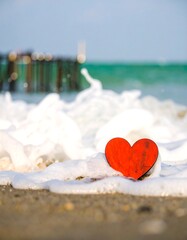 Red wooden heart on sandy shore with ocean waves in background