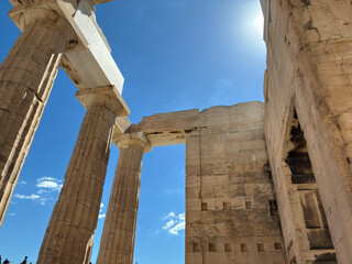 Upward view of Parthenon columns against blue sky and bright sun in Athens, showcasing classical Greek architecture and marble textures.