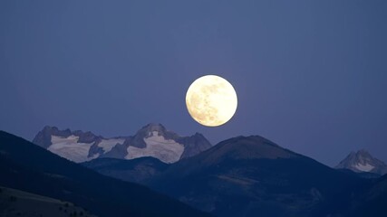 Time-Lapse of a Luminous Full Moon Rising Over a Snowy Mountain Range at Dusk - Powered by Adobe