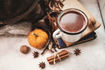 Cozy autumn still life with enamel mug of hot chocolate, pumpkins, vintage books, walnuts, cinnamon sticks, star anise and warm fall clothing, seasonal composition