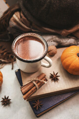 Cozy autumn still life with enamel mug of hot chocolate, pumpkins, vintage books, walnuts, cinnamon sticks, star anise and warm fall clothing, seasonal composition
