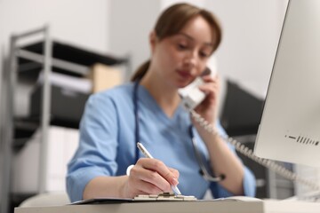 Nurse talking on telephone and taking notes at desk in office, selective focus