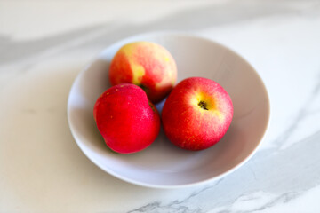 Three red apples on white plate with marble background