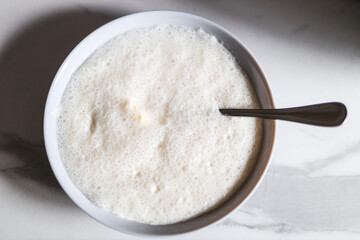 Fresh fermented milk kefir in bowl with spoon on marble countertop
