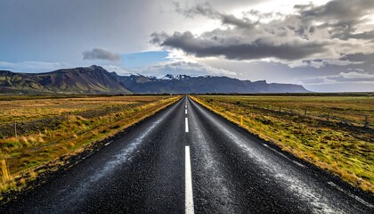 Empty road stretching into a dramatic landscape.  Vast, rugged mountains in the distance under a stormy sky.  Golden grass fields line the highway.  A pristine, white line divides the asphalt